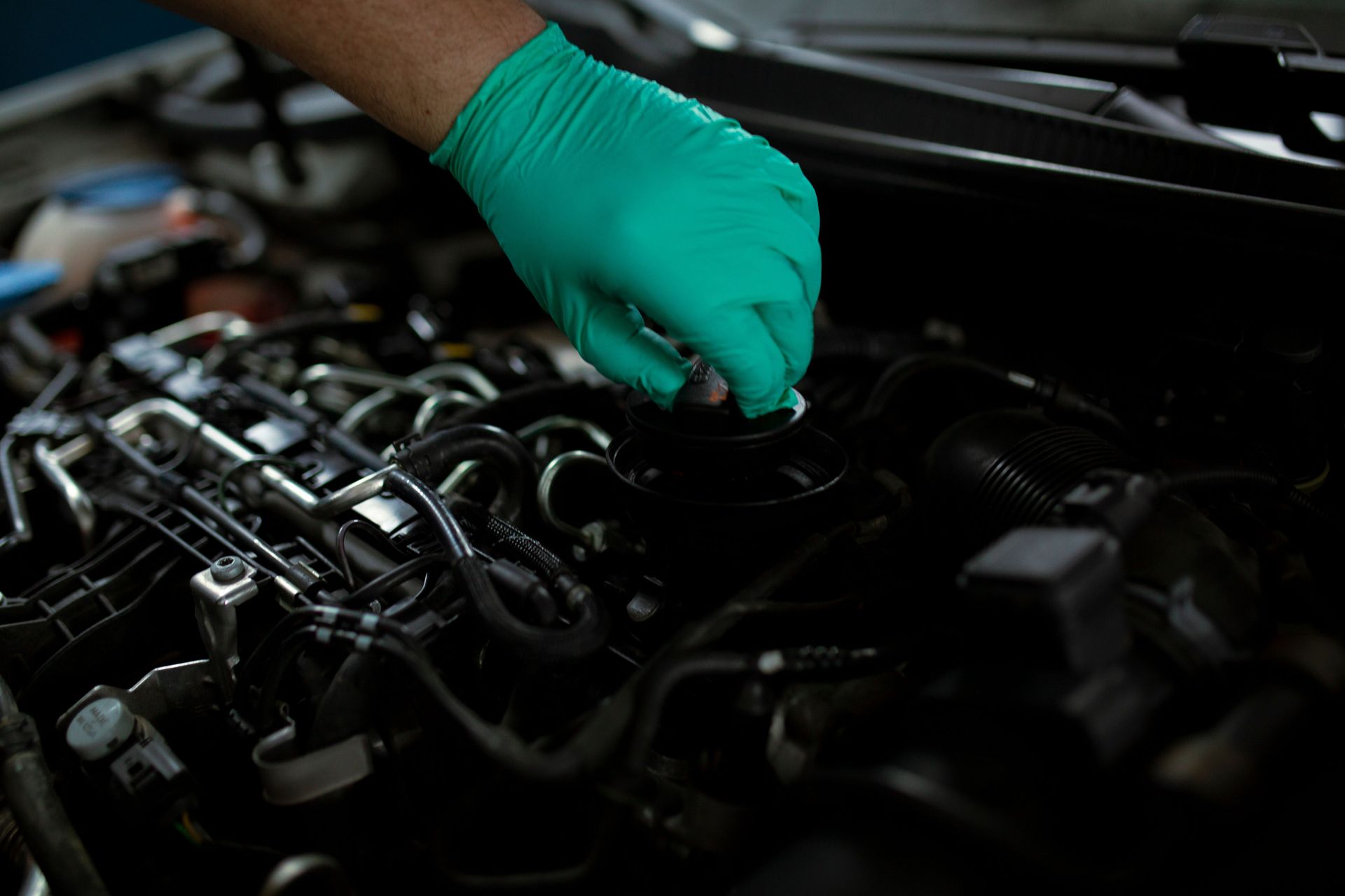 Mechanic wearing gloves changing engine oil in a vehicle. Close-up of a hand working on car maintenance.